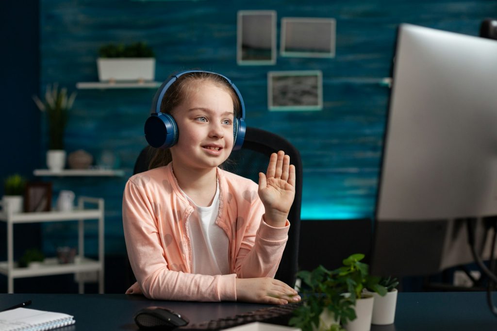 Little schoolchild wearing headset greeting remote teacher during online videocal